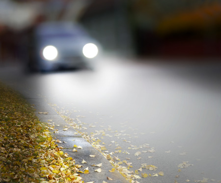 car in blurred motion in city street with switched on headlights in autumnの写真素材