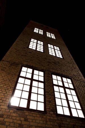 Low angle view of tall building with brick walls and big windows on dark evening skyの写真素材