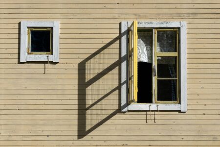 Open window in sunshine casting shadow on wall of old yellow wooden houseの写真素材