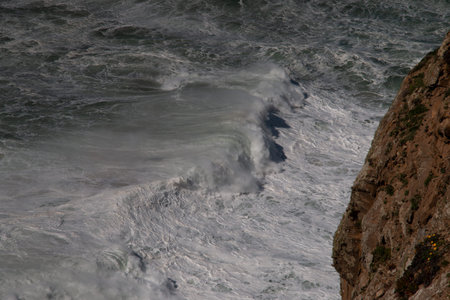 High angle view of troubled water with white froth and a cliff in foreground