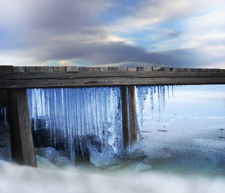 Icicles under wooden jetty in frozen lake on cold winter dayの写真素材