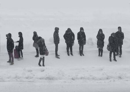 People in dark clothes waiting in heavy snow stormの写真素材