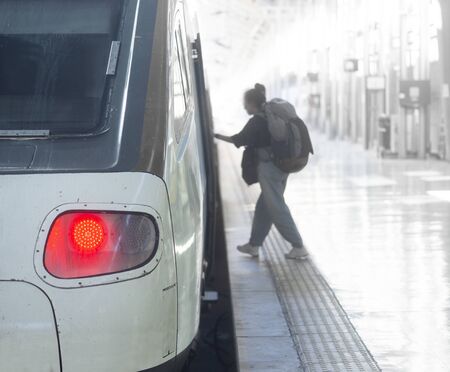 Woman in casual clothes and with big rucksack getting on train in train stationの写真素材