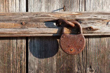 Rusty padlock casting shadow on worn weathered wooden doorの写真素材