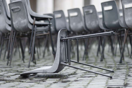 Empty wet plastic chairs outdoors on rainy day, focus on one fallen chair in foregroundの写真素材