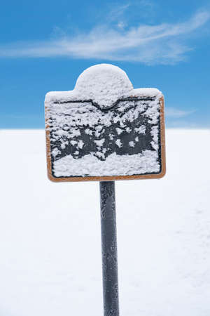 Frozen sign covered in snow and ice crystals in winter landscape with blie skyの写真素材