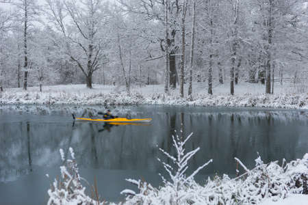 Man paddling in yellow kayak in river in beautiful winter landscape, with rime frost in treesの写真素材