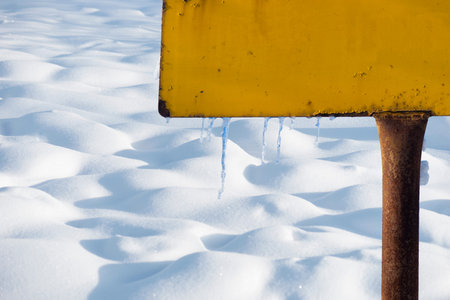 Part of yellow rusty metall sign with icicles in winter landscapeの写真素材
