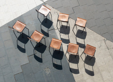 High angle view of empty wooden chairs, casting shadows on concrete floorの写真素材