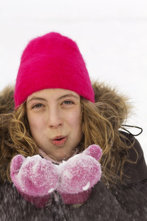 Young teenager with pink tuque blowing fresh snow in the air