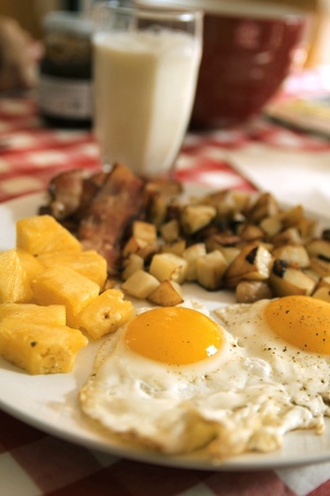 Two eggs sunny side-up with bacon, fruits, and potatoes served with a glass of milk
の写真素材
