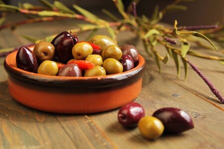 Varitey of olives into in a ceramic bowl  and three olives in foreground on wooden tableの写真素材