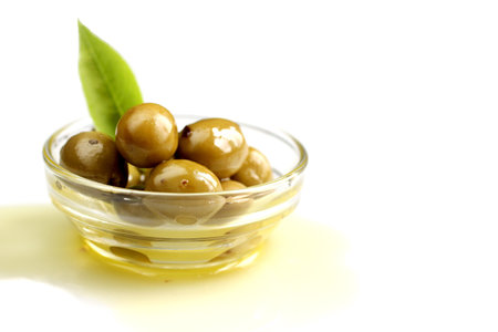Green olive with leaf into olive oil on white backgroundの写真素材