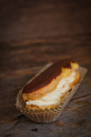 Chocolate eclair in a paper on a wooden surface