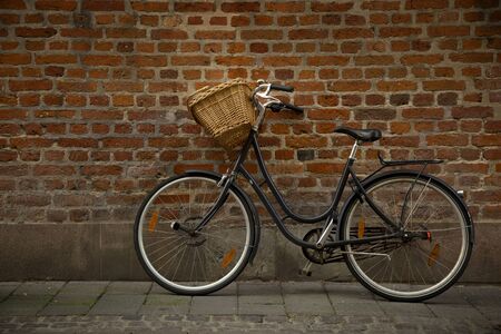 Black bicycle with straw basket along a brick wallの写真素材