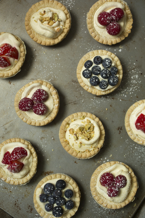 Top view of blueberry, strawberry and pistachios tartlets on  biscuit sheet on a  wooden tableの写真素材