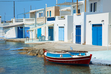 Fishing boat in front of a blue fishing village in Milos island in Greeceの写真素材