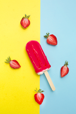 Strawberry popsicle with fresh strawberry on a yellow and blue backgroundの写真素材