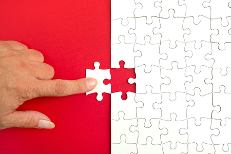 Hand holding piece of white puzzle on blue background. Business and team work conceptの写真素材