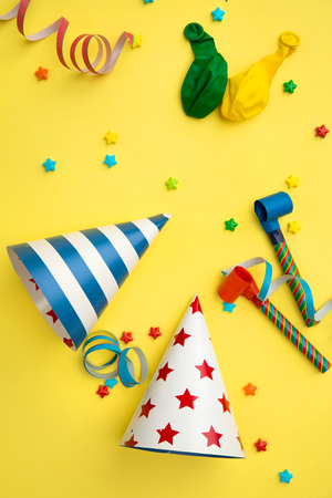 Birthday items for a party like hats, balloons and candles on a yellow backgroundの写真素材
