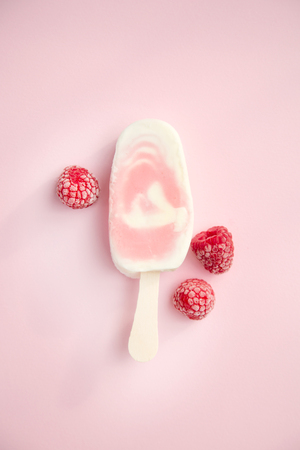 Berry sorbet and yogurt ice lolly with raspberry on a pale pink backgroundの写真素材