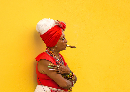 HAVANA-CUBA- DEC 4, 2018:  Woman with a cigar in her mouth with a yellow background letting tourists take photos of her for a few pesos in Havana street in Cubaのeditorial素材