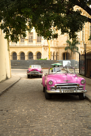 HAVANA-CUBA- DEC 4, 2018:  Two classic American vintage convertible cars in pink and colonial architectural building in Old Havana in Cubaのeditorial素材