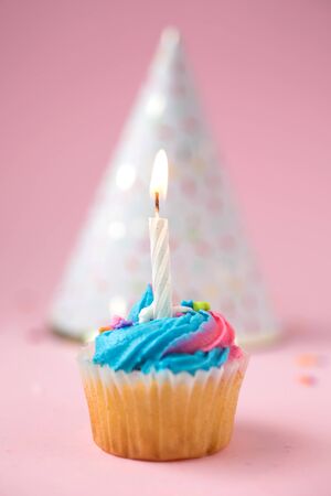 Cupcake with blue and pink icing and birthday hat on a pink backgroundの写真素材