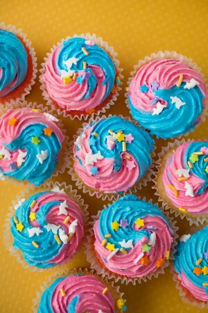Top view of cupcakes with blue and pink icing on a yellow backgroundの写真素材