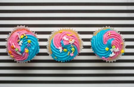 Three cupcakes with blue and pink icing on a black and white lined backgroundの写真素材