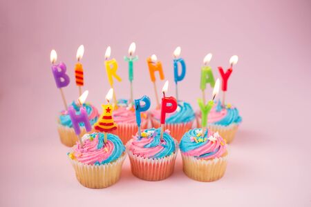 Cupcakes with blue and pink icing and happy birthday candles on a blue backgroundの写真素材