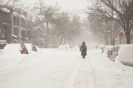 Anonyme woman walking in a street covered of snow during a heavy snowstorm in Montreal in Canadaの写真素材