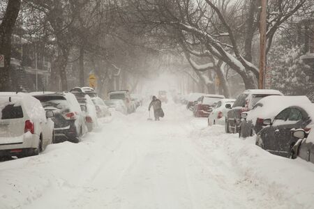 Man with shovel walking in a street covered of snow and cars full of snow in a street during a snowstorm in Montreal in  Canadaの写真素材