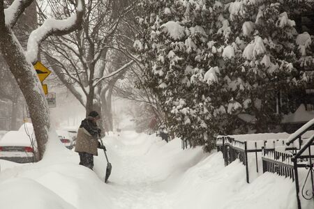 MONTREAL-CANADA, 7th february 2020: Man with shovel cleaning the sidewalk and alley during a major snowstorm, more than 40 cm had fallen in Montreal in Canada.の写真素材