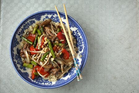 Colored vegetables saute in a blue bowl and chopsticks on a textured backgroundの写真素材