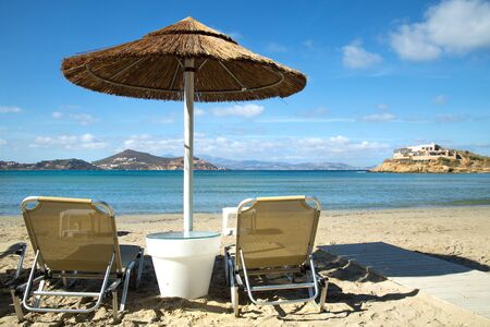 Sunbathing chairs on a beach with turquoise ocean and a straw parasol in Greeceの写真素材