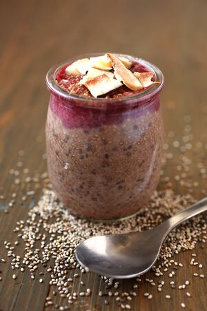Healthy chocolate chia pudding surround by chia seeds with berry coulis on top and coconut on a woodenの写真素材