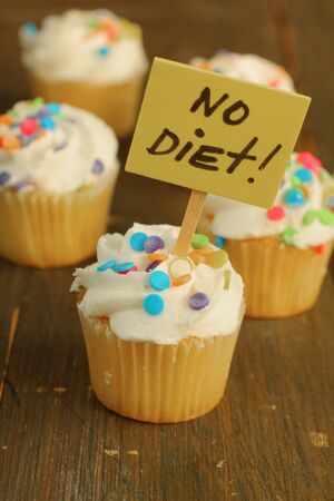 Vanilla cupcake with candies on top and no diet sign on it on a woodenの写真素材