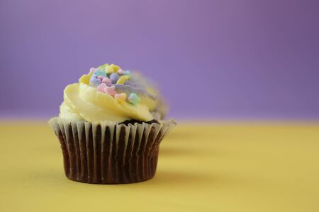  Easter yellow and lilac chocolate cupcake with candies on a yellow and purple backgroundの写真素材