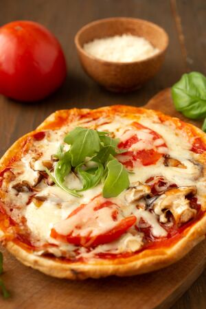 Homemade pizza with tomato, mushrooms, peppers and fresh herbs basil and arugula presented on a wooden board with pizza cutterの写真素材