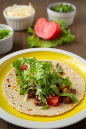 Yellow plate mexican beef tacos with condiment tomato, lettuce, coriander, cheese on a wooden tableの写真素材