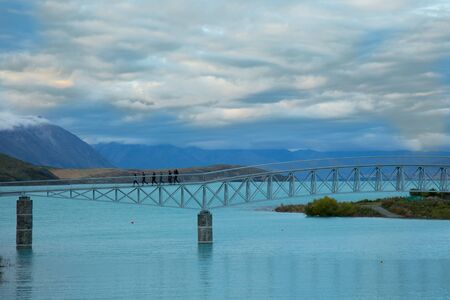 Bridge over turquoise water Tekapo lake with a dramatic sky in southern island in New Zealandの写真素材