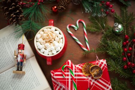 Marshmallow on top of a hot chocolate in a red cup surrounded by christmas candies, gifts and pine treesの写真素材