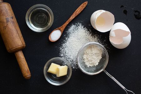 Ingredient for making delicious pancake, pie or cake( eggs, flour, butter, salt and baking powder) on black background and a rolling pinの写真素材