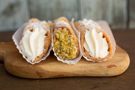 Three italian  cannolis nature and with pistachio on a cupboard on a wooden backgroundの写真素材