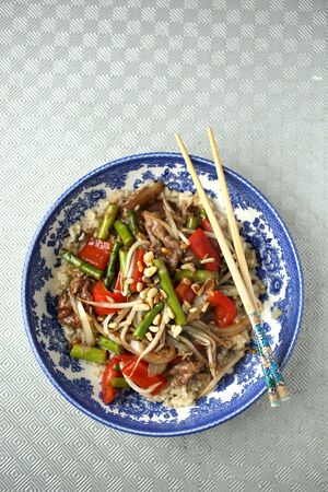 Colored vegetables saute in a blue bowl and chopsticks on a textured backgroundの写真素材