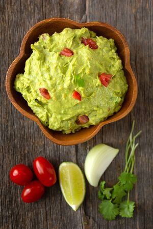 Top view of a bowl of traditional mexican guacamole with lime, tomatoes, onion and coriander on a wooden backgroundの写真素材