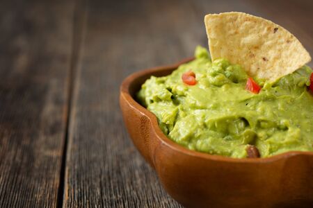 Bowl of traditional mexican guacamole with nachos chips on a wooden backgroundの写真素材