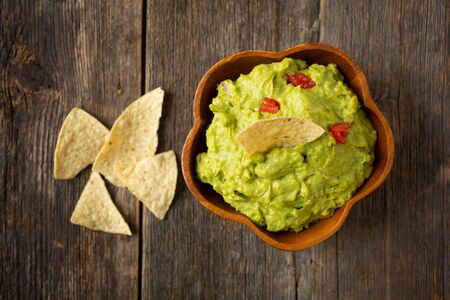 Close up of a bowl of traditional mexican guacamole with nachos chips on a wooden backgroundの写真素材