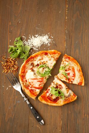 Homemade pizza with tomato, mushrooms, peppers and fresh herbs basil and arugula with fork and pepperの写真素材